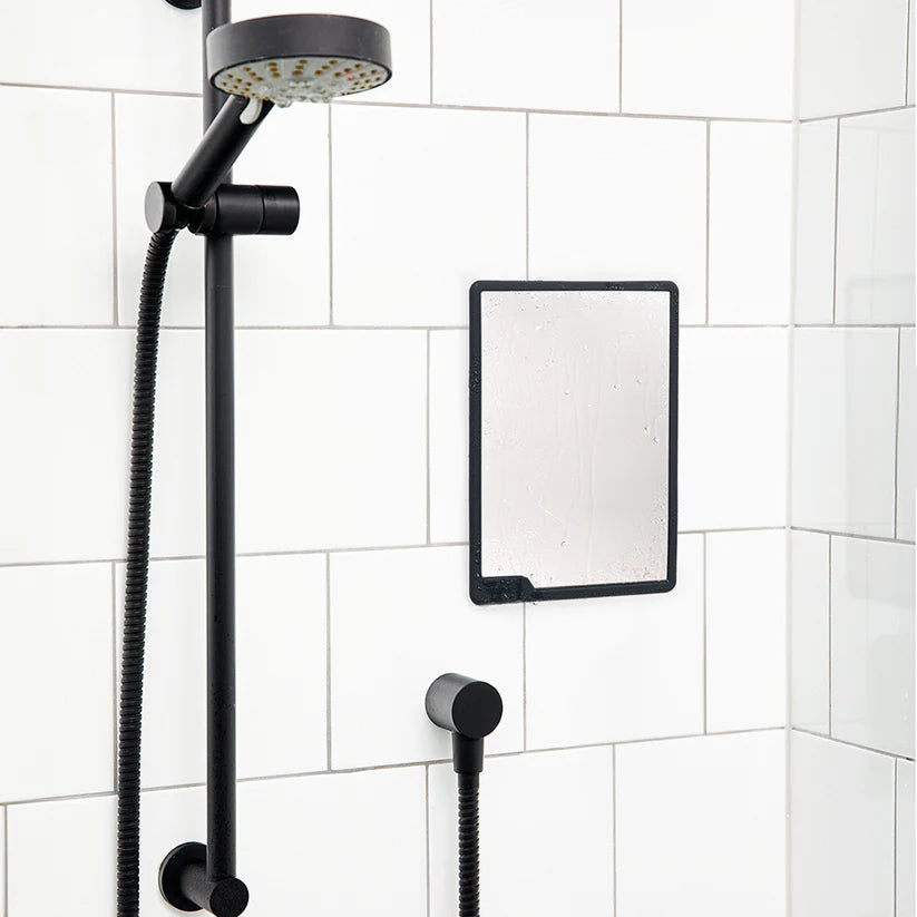 Charcoal shower mirror mounted on white tiles beside black shower head — Adventure Awaits