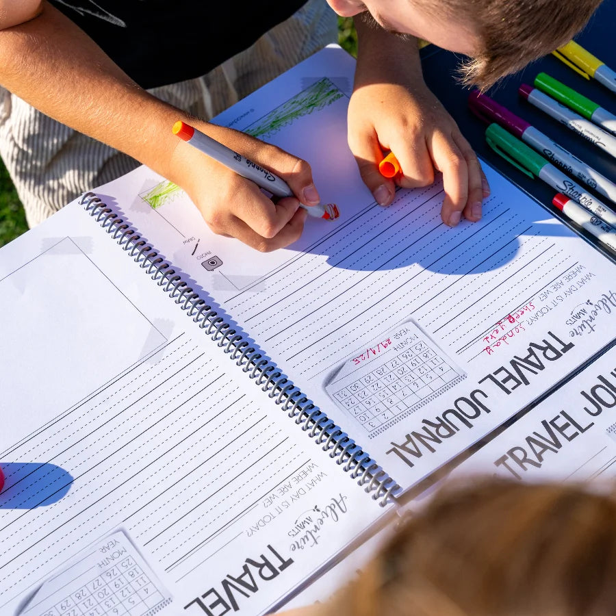 Young boy drawing in the kids travel journal out in the sun 