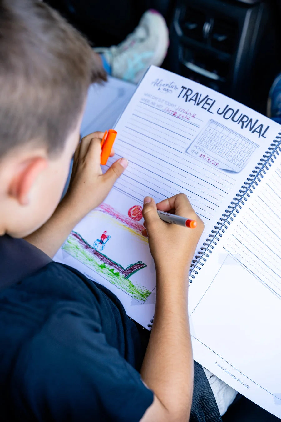 Young boy drawing in his kids travel journal in the car 
