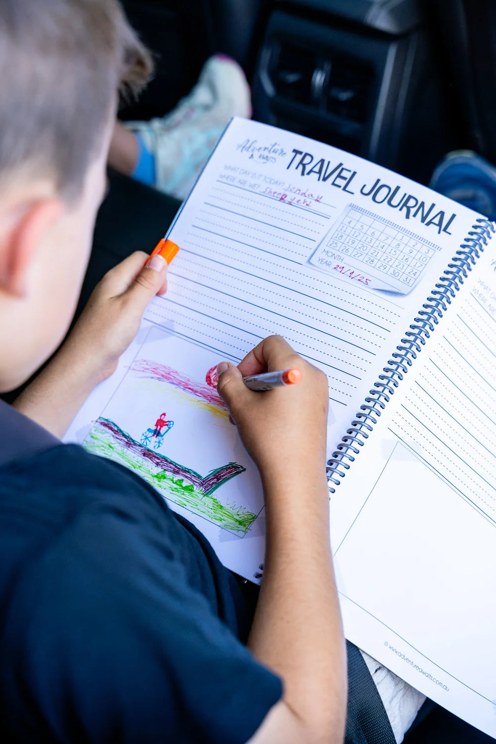 Young boy in the backseat on car drawing and colouring into the kids travel journal 