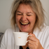 Woman laughing joyfully while holding a white mug with 'Mug' printed on it.