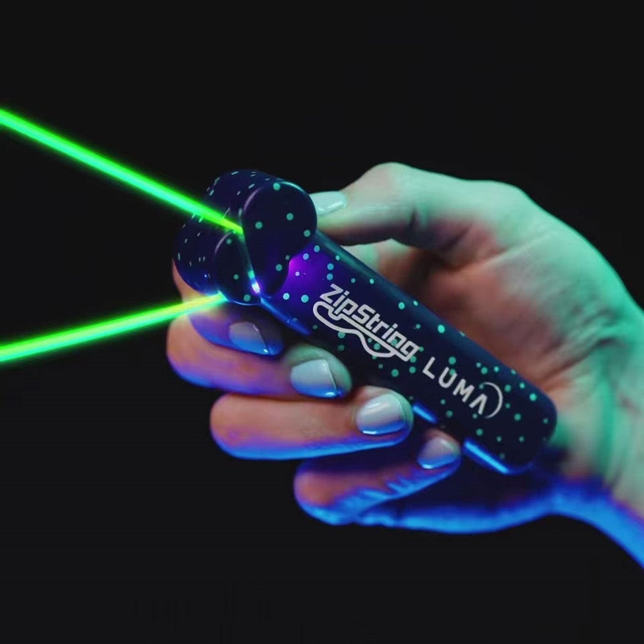Close-up of the ZipString Luma handheld launcher in use, with glowing green strings shooting from the device against a dark background.