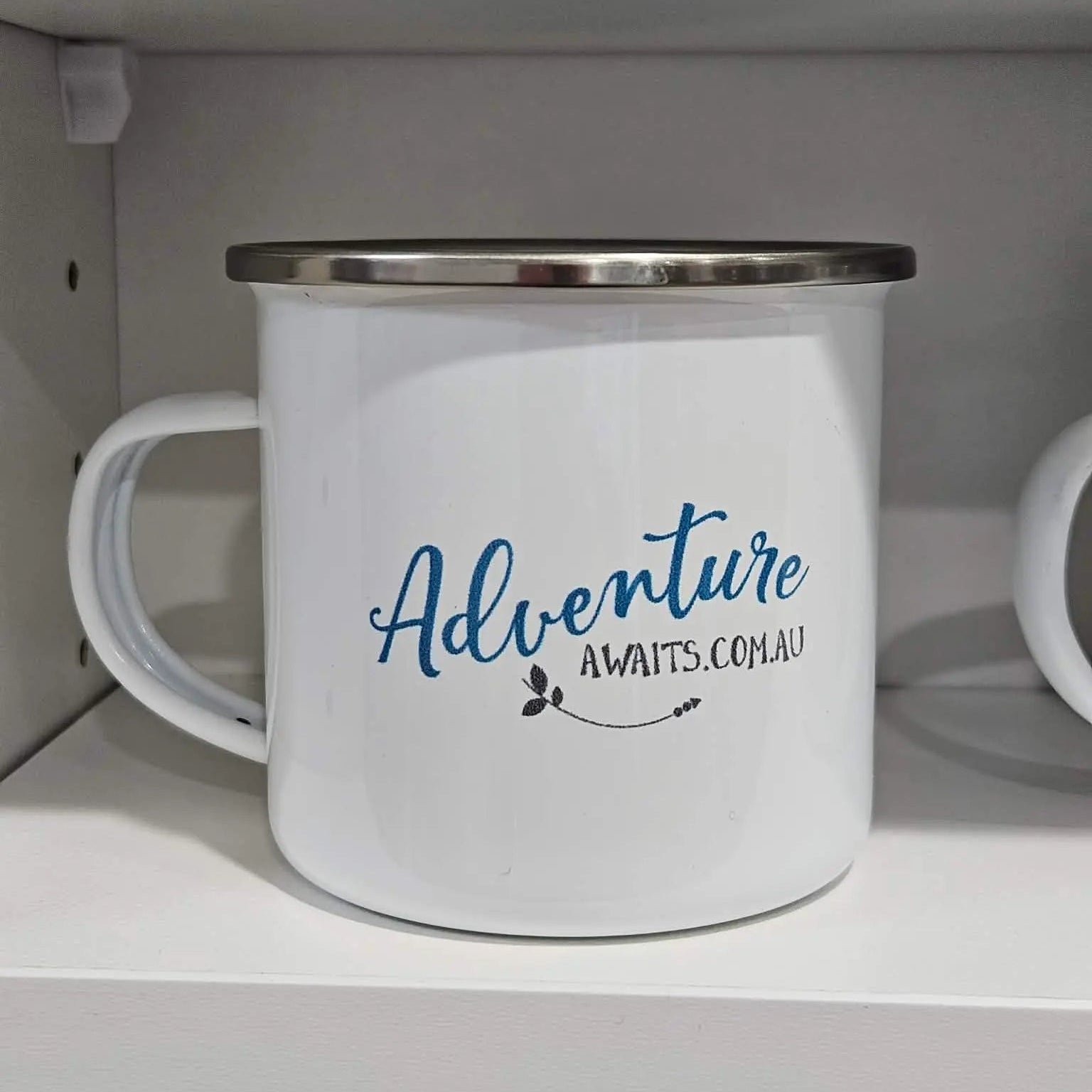 White mug with 'Adventure Awaits' text on a shelf