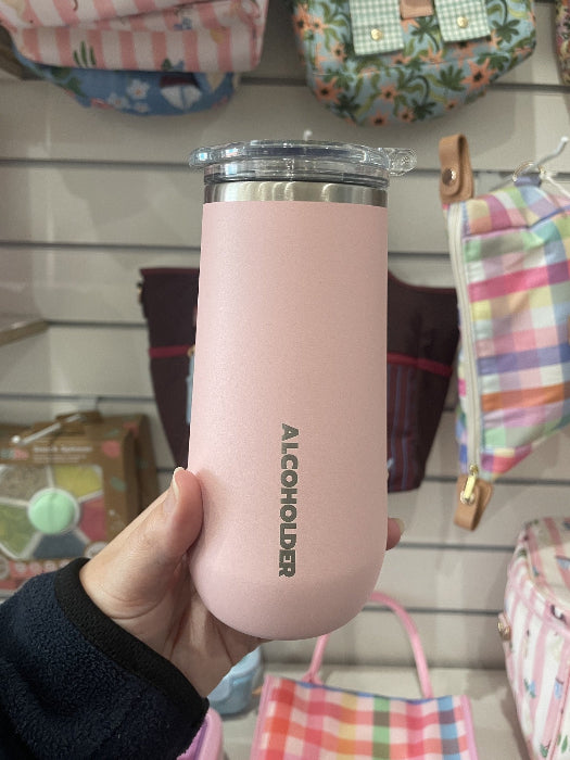 hand holding pink insulated wine tumbler with clear lid and Alcoholder branding, stylish reusable drinkware displayed in retail store Adventure Awaits