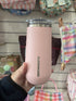 hand holding pink insulated wine tumbler with clear lid and Alcoholder branding, stylish reusable drinkware displayed in retail store Adventure Awaits