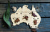 Australia-shaped wooden wine charm set with native animal markers displayed on rustic timber — Adventure Awaits