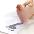 adult holding baby's foot near inkless kit footprint