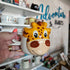 Hand holding a mug with a cartoon giraffe design against a blurred store background