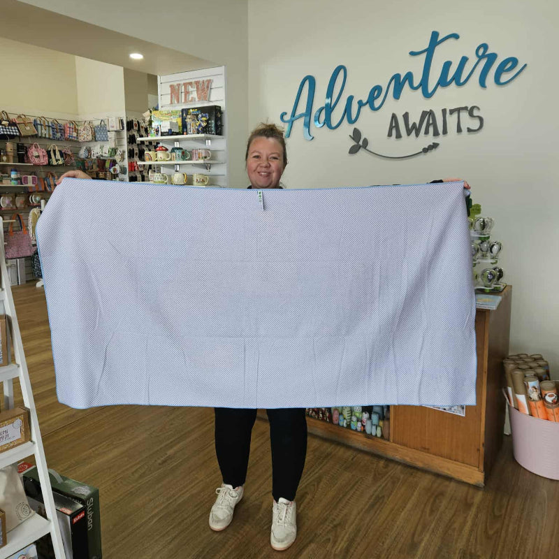 Person holding a large towel in a store with 'Adventure Awaits' sign.