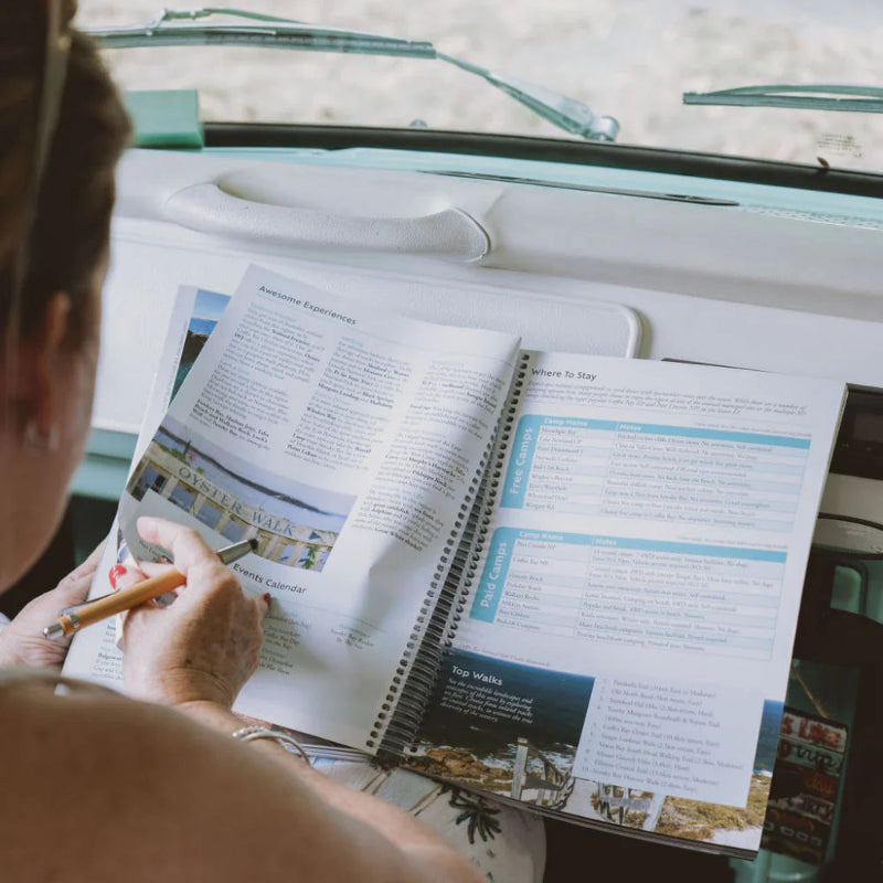 Traveller writing notes in Hema Big Lap Bible inside vehicle, Australian road trip guide Adventure Awaits