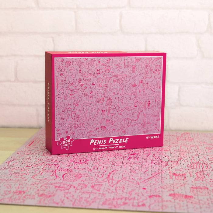 Pink Penis Puzzle box displayed in front of the completed 1000-piece illustrated jigsaw — Adventure Awaits