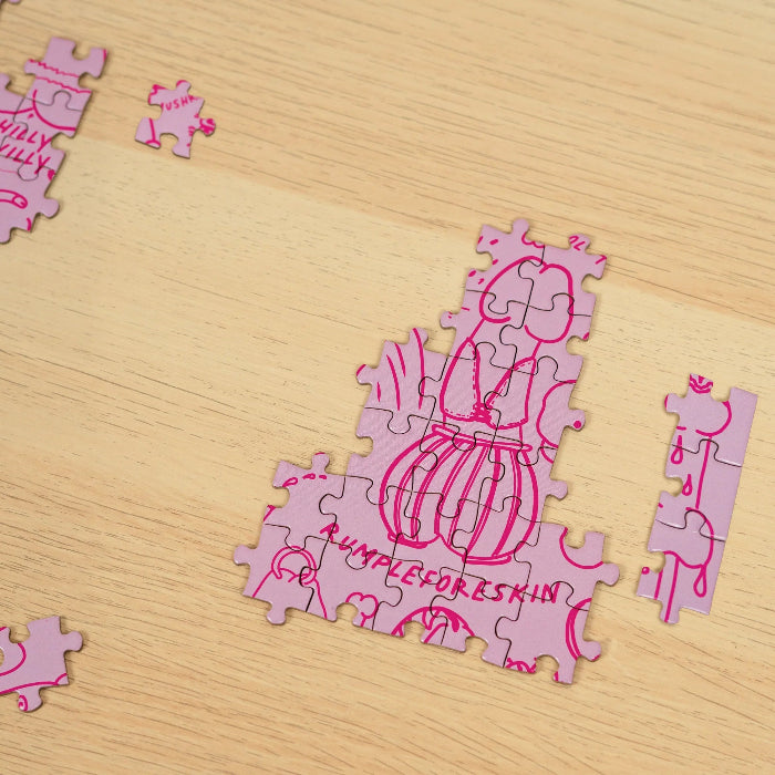 Partially completed pink Penis Puzzle with cheeky illustrated jigsaw pieces on a timber table — Adventure Awaits