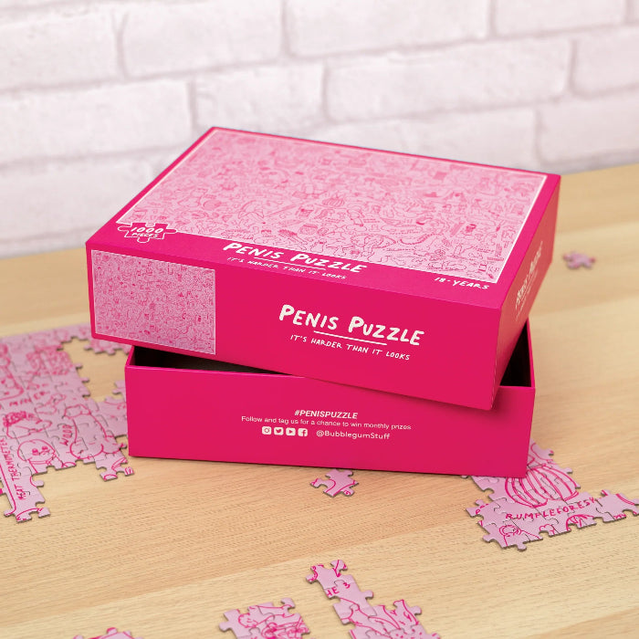 Open pink Penis Puzzle box with 1000-piece jigsaw pieces scattered across a timber table — Adventure Awaits