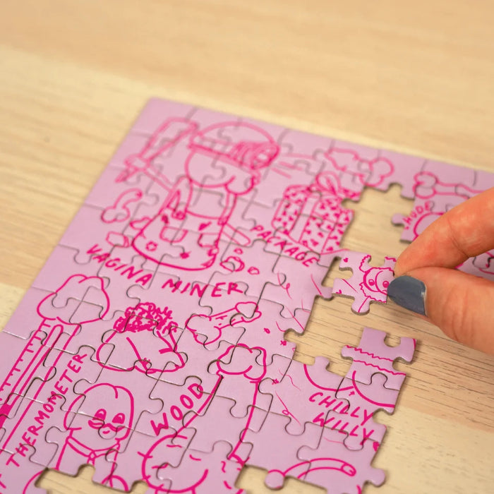 Hand places a piece into the pink Penis Puzzle featuring cheeky illustrated designs — Adventure Awaits