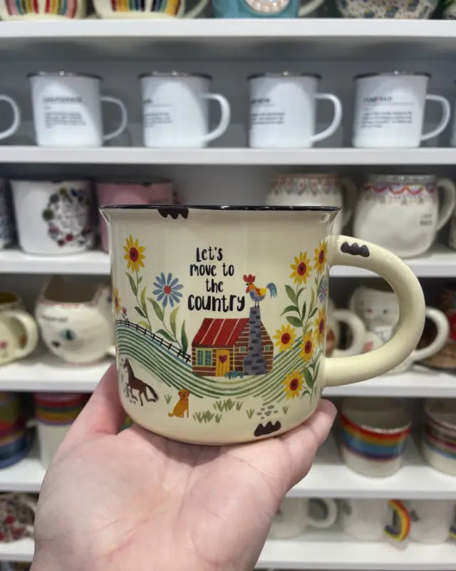 Hand holding a Let’s Move to the Country camp mug with cottage and floral design — Adventure Awaits