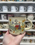 Hand holding a Let’s Move to the Country camp mug with cottage and floral design — Adventure Awaits