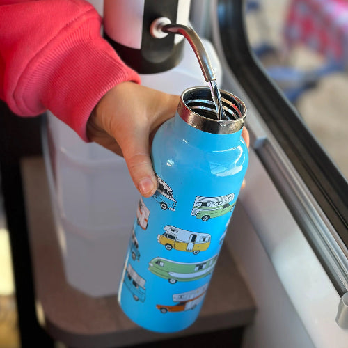 Hand holding a blue water bottle with camper designs near a window.