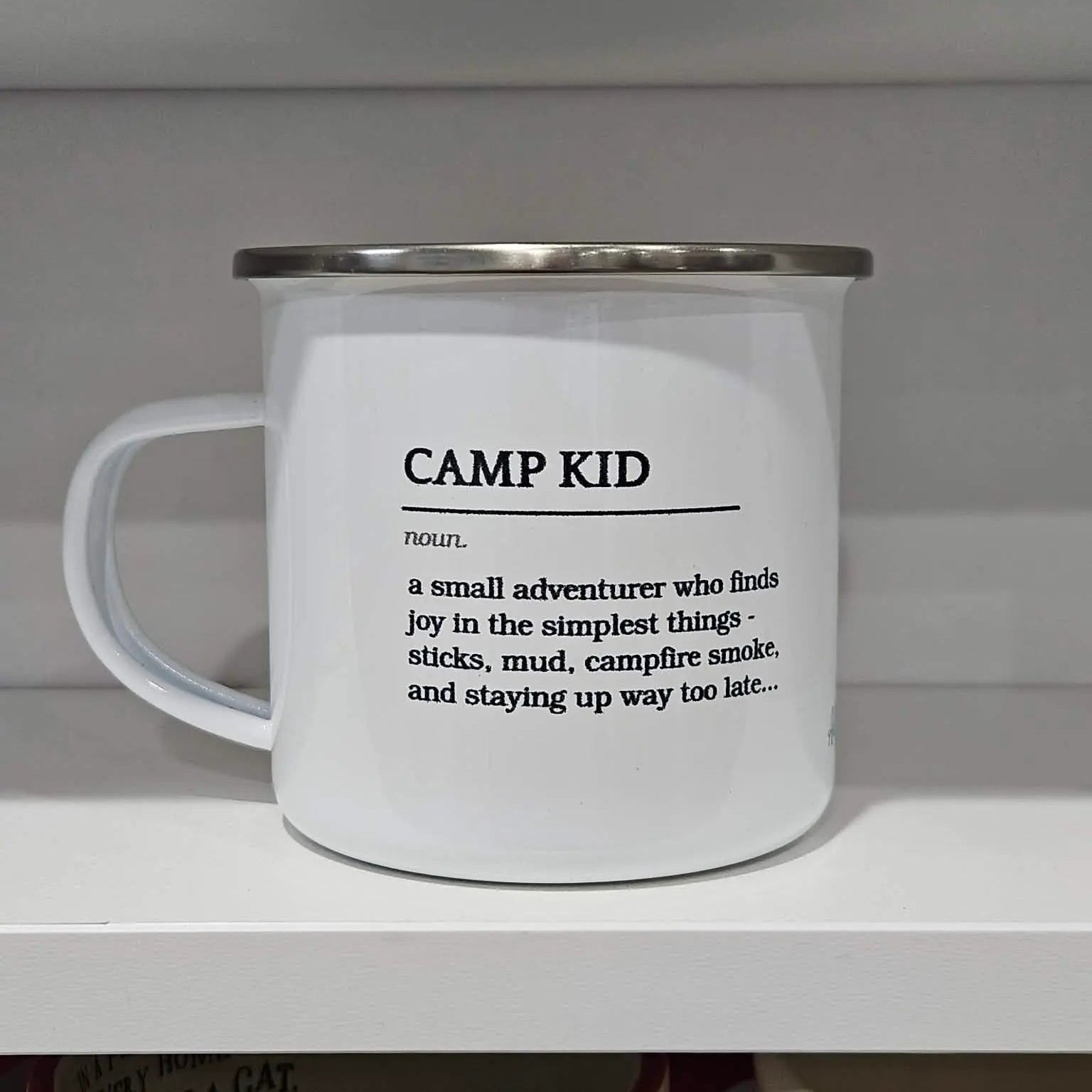 White mug with 'CAMP KID' definition text on a white shelf