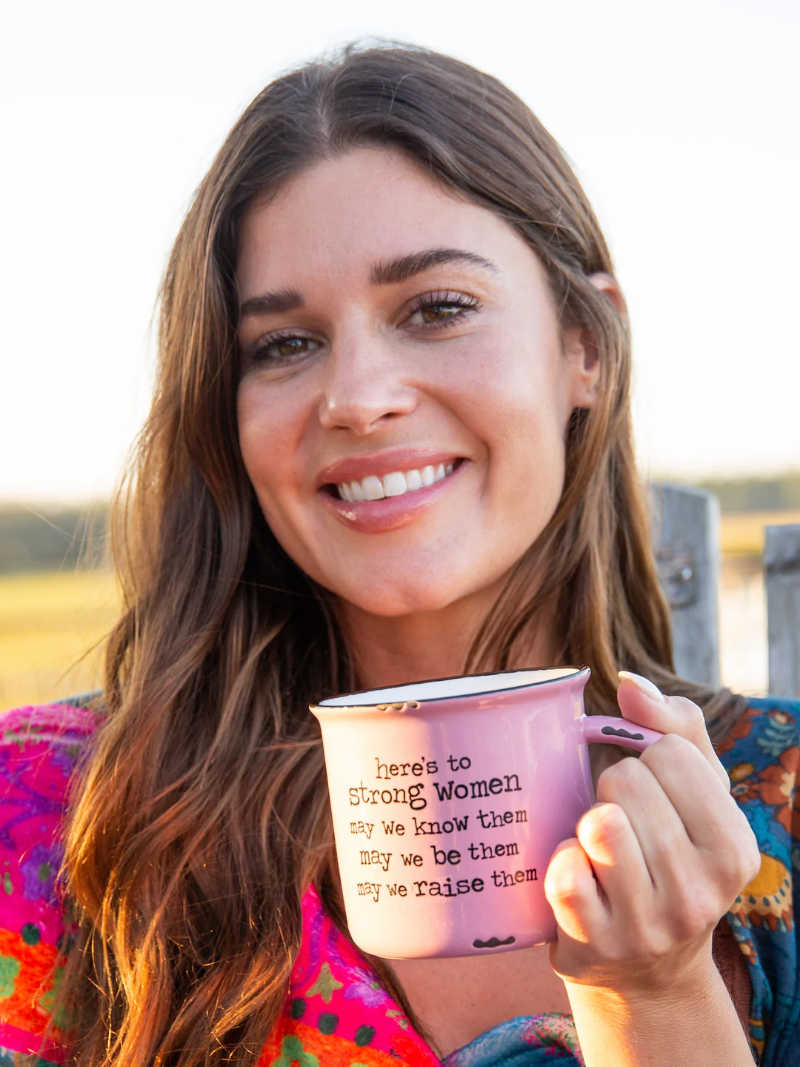 Woman holding a pink mug with text, standing outdoors.