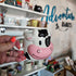 Small pink and white cow-shaped device held in a hand with a blurred background