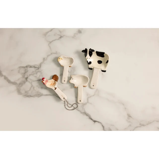 Ceramic cow, pig, sheep and rooster measuring spoons arranged on a marble bench — Adventure Awaits