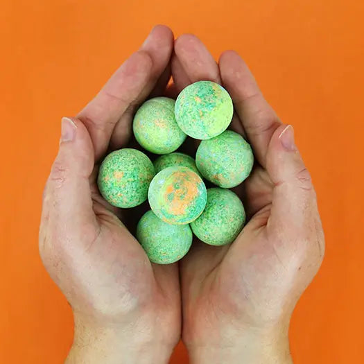 Hands holding green Dino Poop bath bombs with orange speckles — Adventure Awaits