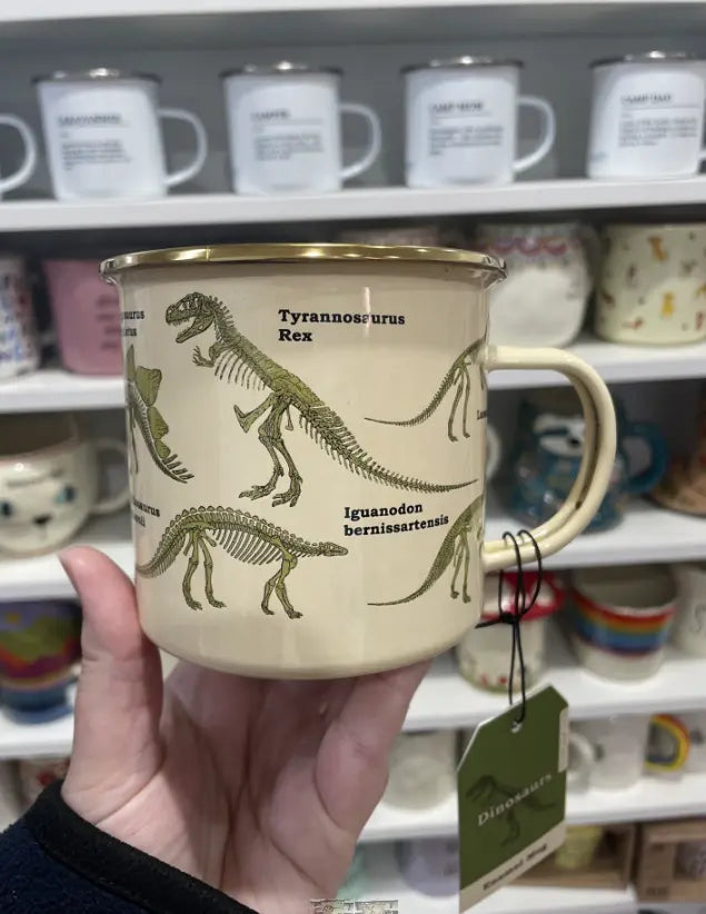 Cream enamel dinosaur mug held in store with skeleton illustrations and gift tag Adventure Awaits