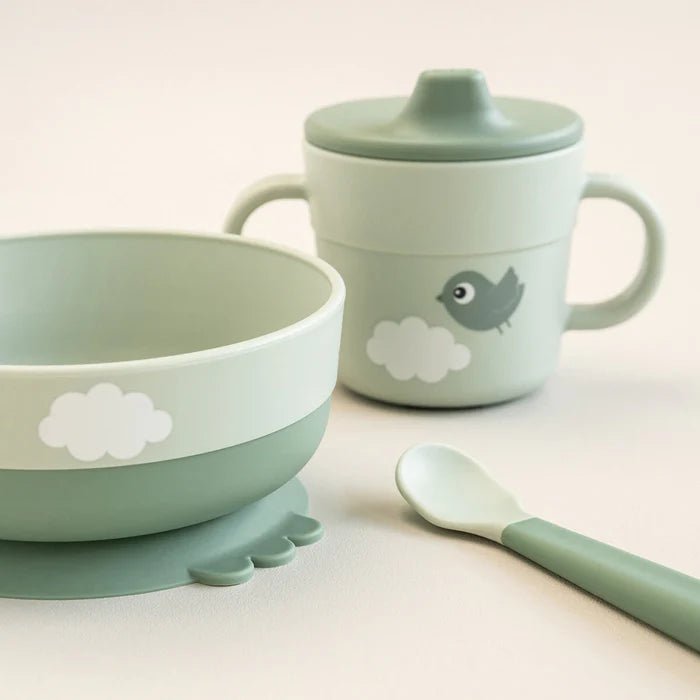 Close up of baby feeding set with suction bowl, spoon and handled cup with lid in soft green tones, perfect for easy mess free mealtimes at home or travel Adventure Awaits