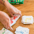 Hands sorting Dutch Blitz  playing cards on a wooden surface with a box in the background