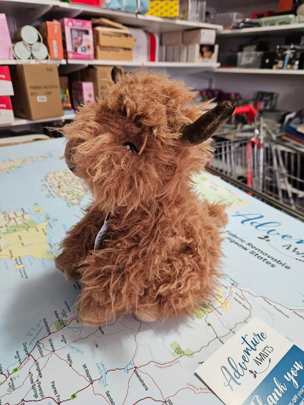 Plush highland cow toy on a map with shelves in the background