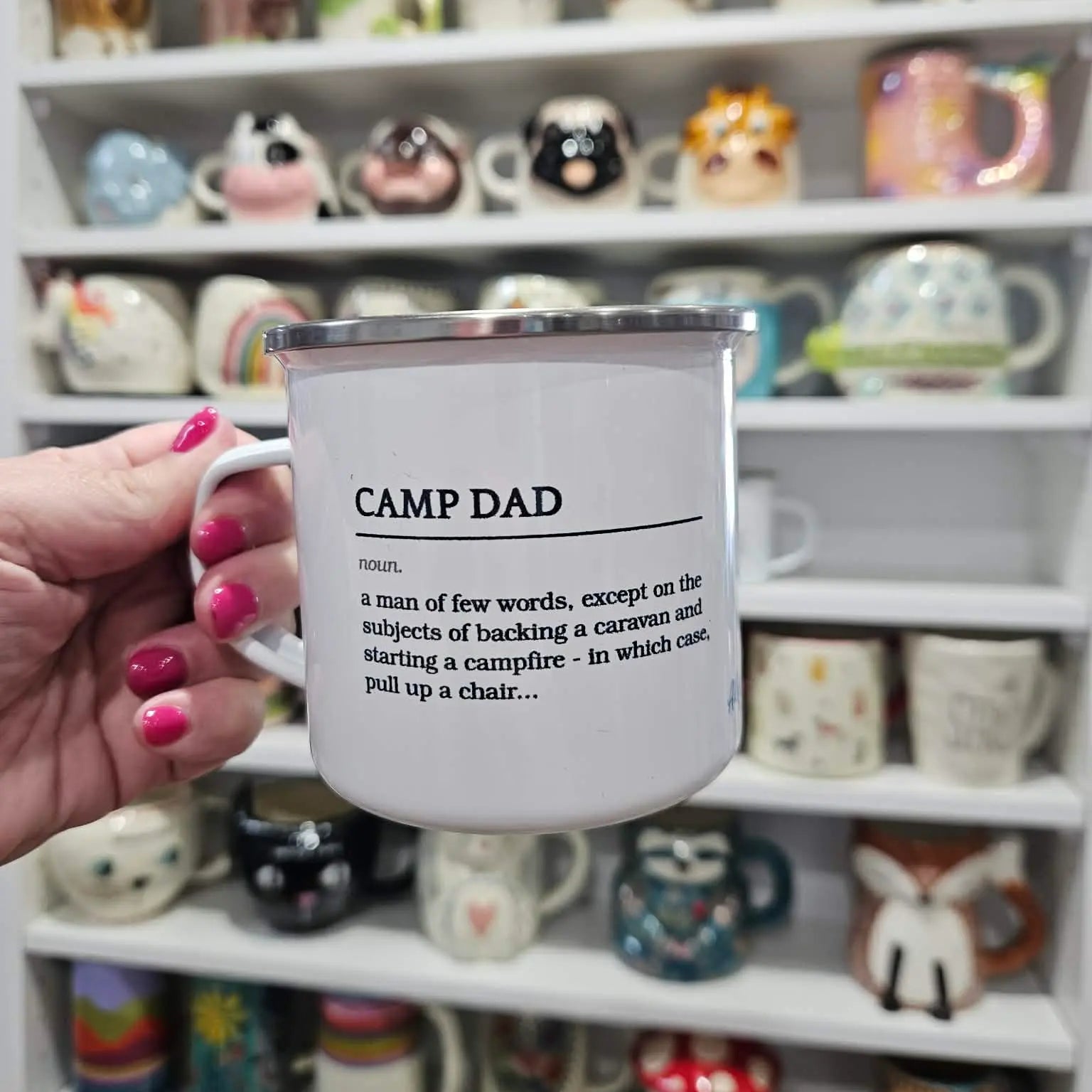Person holding a mug with 'Camp Dad' definition in front of a shelf of various mugs.