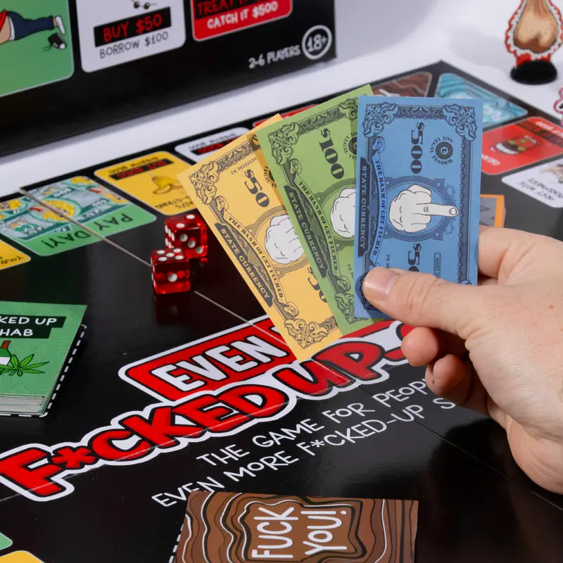 Board game with cards and dice on a table, featuring explicit language.