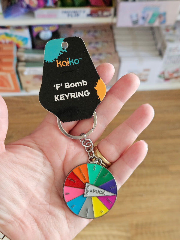 Hand holding a keychain with a colorful wheel and a black keyring with text.