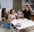 Three adults laughing while playing Fidget About It with colourful puzzle balls around a coffee table — Adventure Awaits