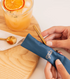 Hand sliding gold Frank Green reusable straw into blue carry pouch beside iced drink — Adventure Awaits