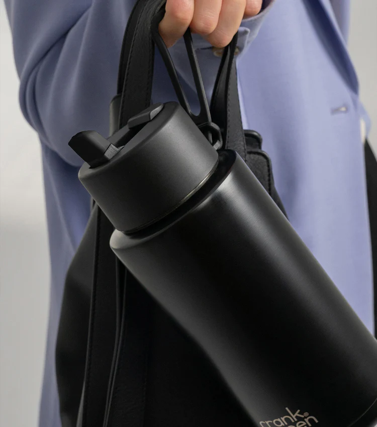 Midnight Frank Green bottle with flip straw lid held alongside a handbag — Adventure Awaits