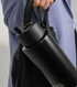 Midnight Frank Green bottle with flip straw lid held alongside a handbag — Adventure Awaits