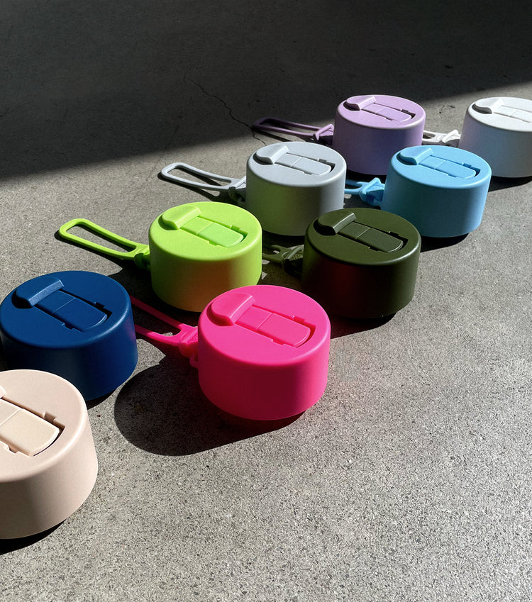 Assorted colourful Frank Green bottle lids with matching straps on concrete — Adventure Awaits