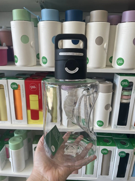 Hand holding clear frank green bottle with black push-button lid in store display — Adventure Awaits