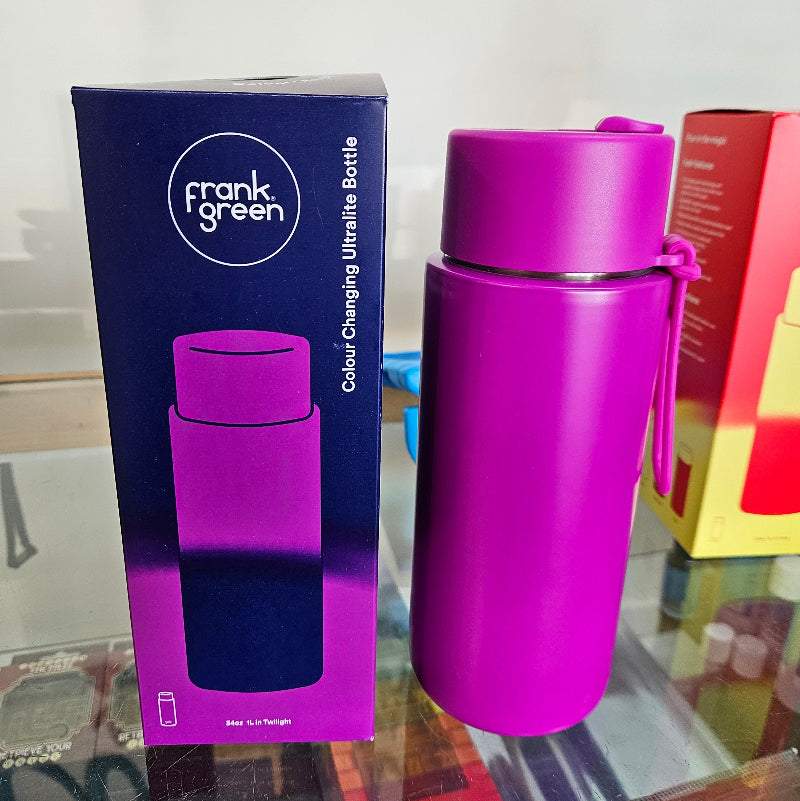 Purple reusable water bottle with packaging on a reflective surface