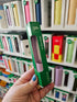 Hand holding a green lip gloss holder with a blurred background of shelves with lip products.