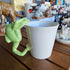 White mug with a green frog handle on a wooden surface