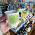 Frog-themed mug held in a hand with a store interior in the background