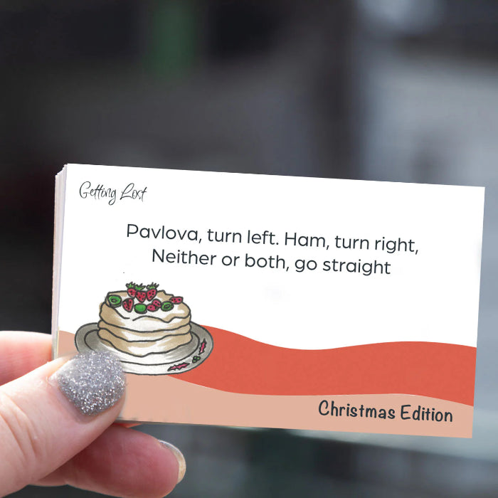 Hand holds a Getting Lost Christmas Edition direction card with pavlova, ham and route prompts, Adventure Awaits