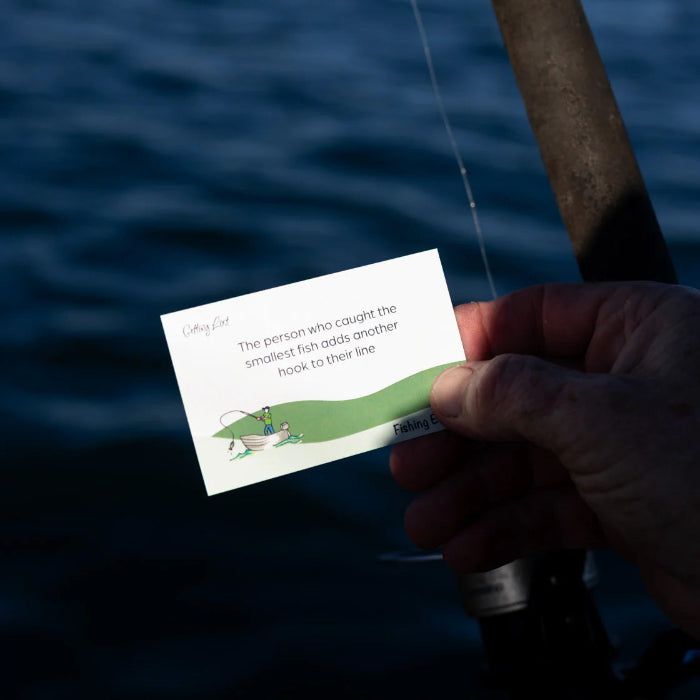 Hand holds a Getting Lost Fishing Edition card adding another hook beside a fishing rod, Adventure Awaits