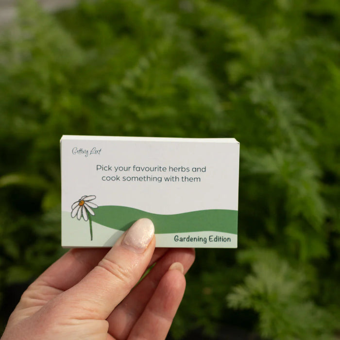 Hand holds a Getting Lost Gardening Edition card prompting favourite herbs to pick and cook, Adventure Awaits