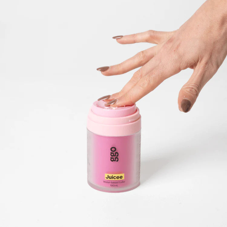 Hand pressing the pump on pink GGO Juicee 100 ml water-based lubricant, Adventure Awaits