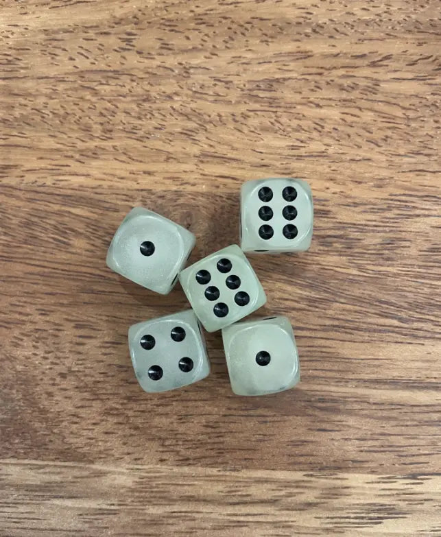 Five glow-in-the-dark dice with black dots on a wooden tabletop — Adventure Awaits