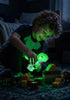 Child playing with green glowing dinosaur toy in a dark bedroom scene — Adventure Awaits