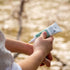 Hand applying a tube of Good Riddance Rescue balm to a person's arm with a blurred natural background